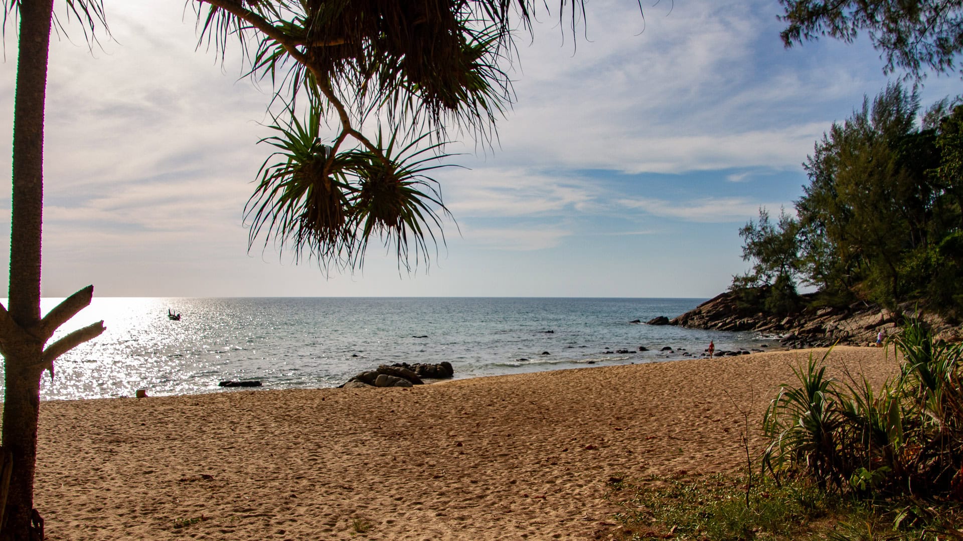 Naithon Beach Phuket quiet corner of the bay with golden sand, scattered rocks and pandanus trees looking out over calm afternoon sea.