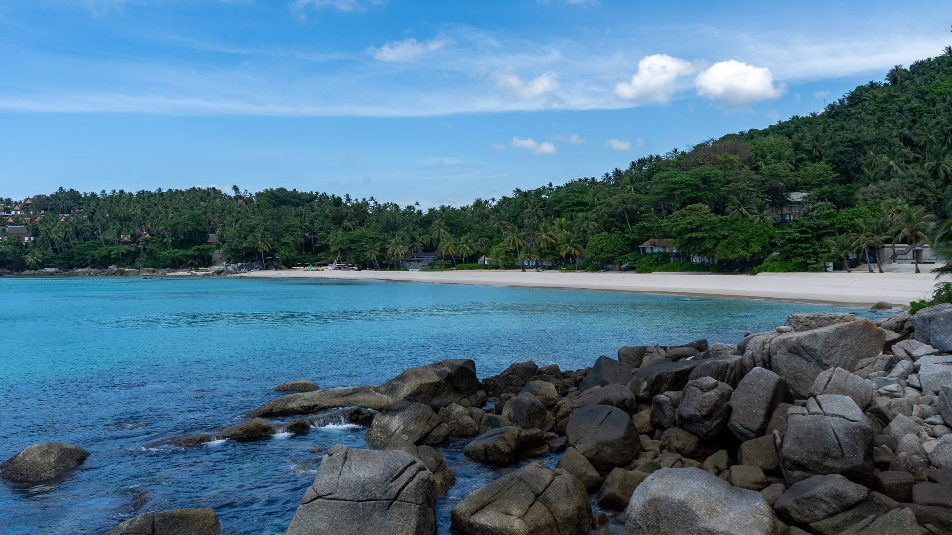 Rocky foreground with wide turquoise bay and forested hillsides.