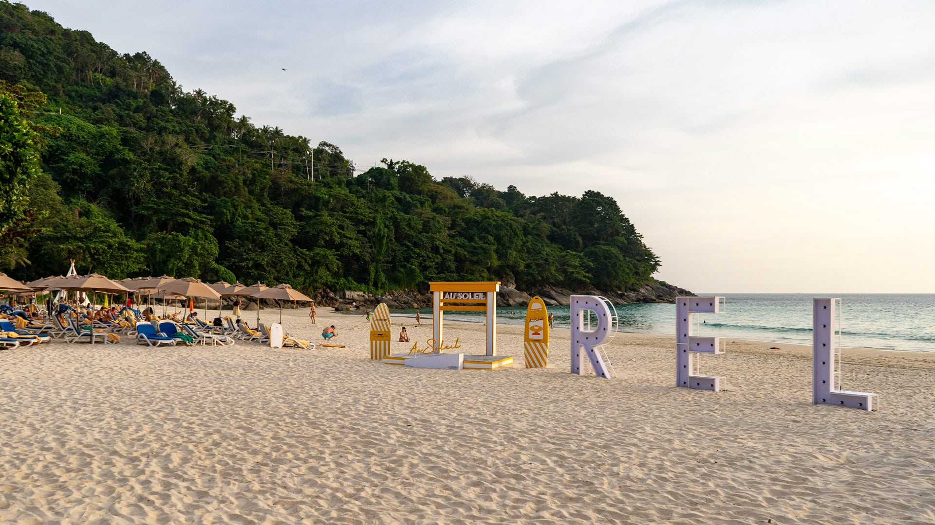 Karon Noi Beach Phuket with sun loungers, beach umbrellas, and a forested hillside behind the sand