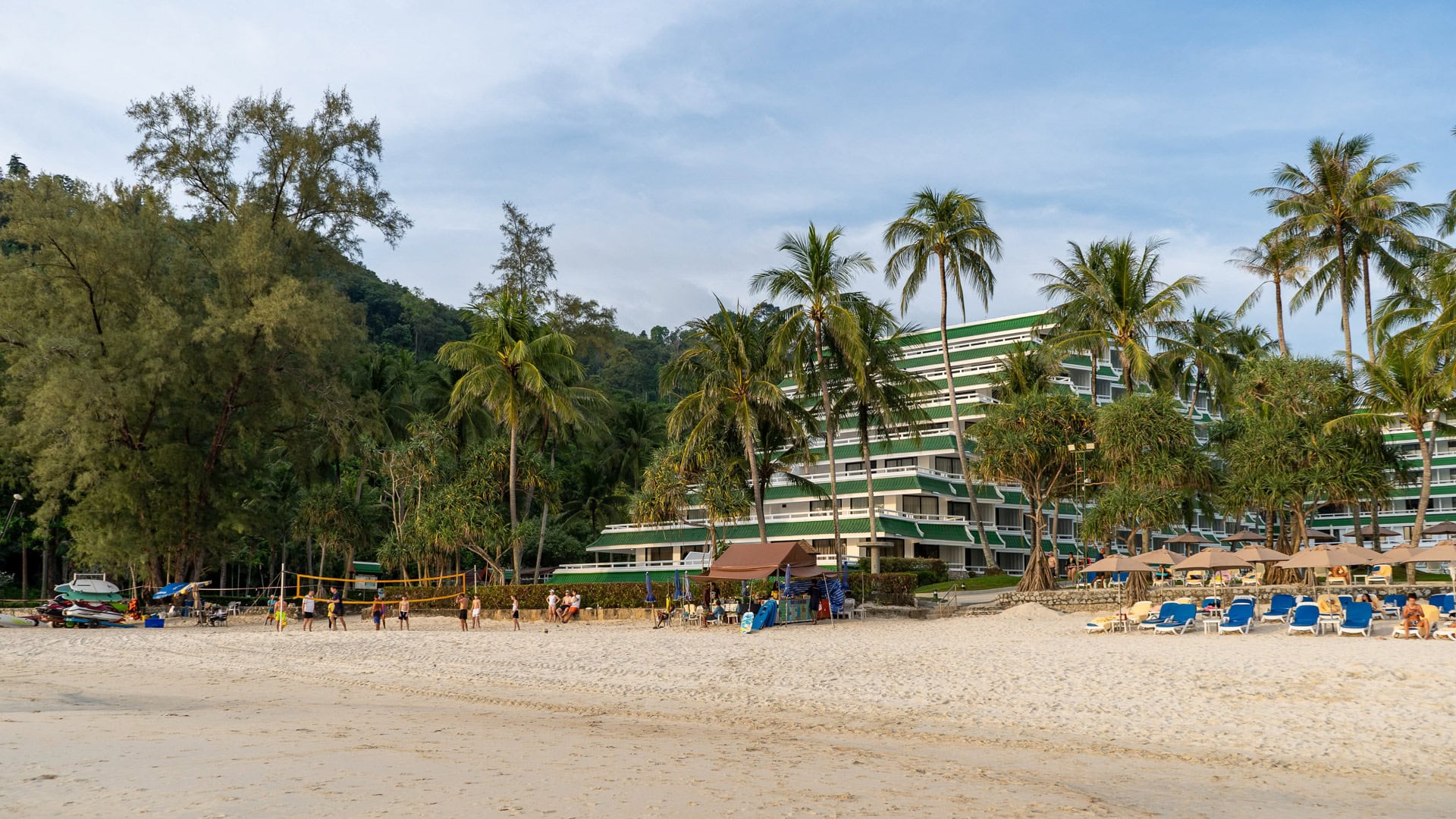 Karon Noi Beach Phuket with beachfront resort building, palm trees, volleyball net, and sun loungers on the sand